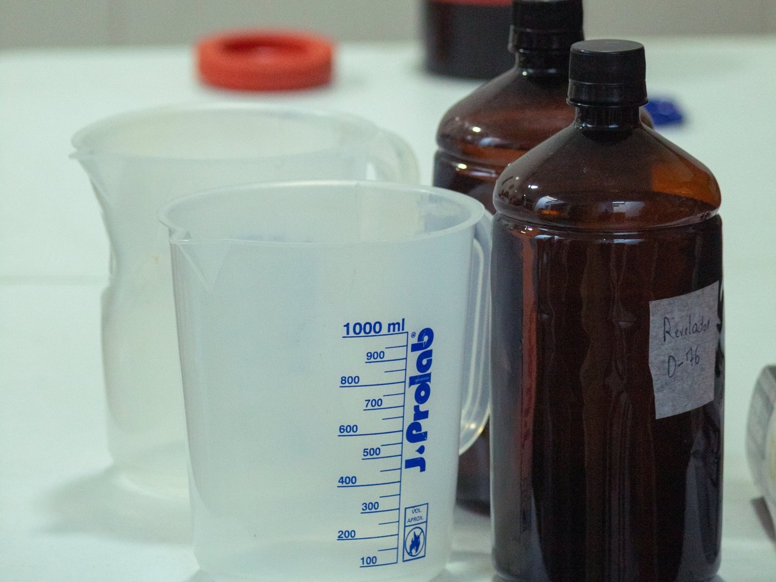 Frascos de revelador D-76 e jarras de medição na bancada do laboratório do Cafeína Lab